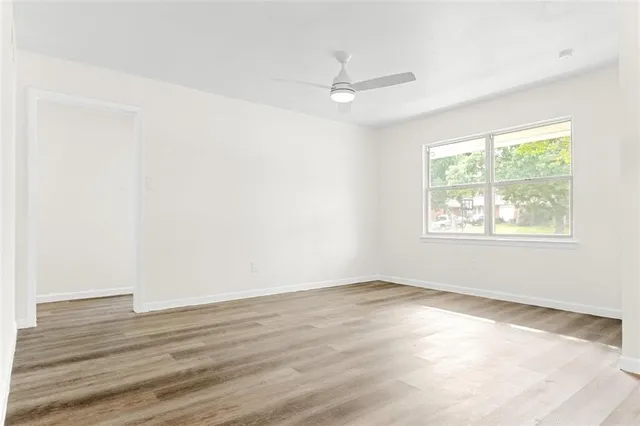 an empty room with wooden floor chandelier fan and windows