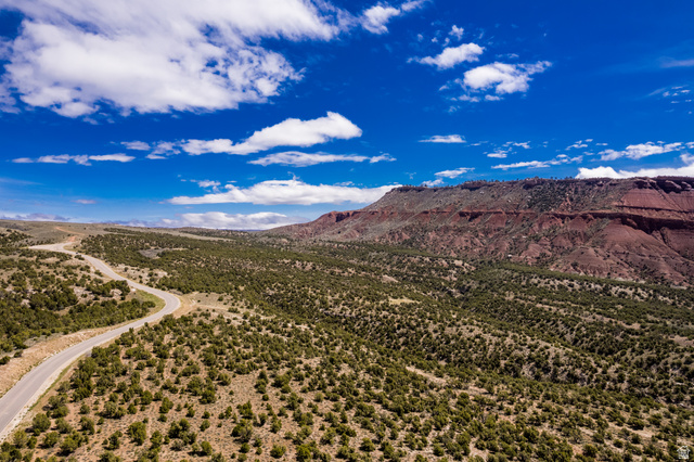 2650 Taylor Mountain Road, Unit REMARK Vernal, UT 84078 - Photo 1 of 7 Sweeping landscape featuring a winding paved road, red rock formations, abundant low-lying green vegetation, and a clear blue sky with scattered clouds