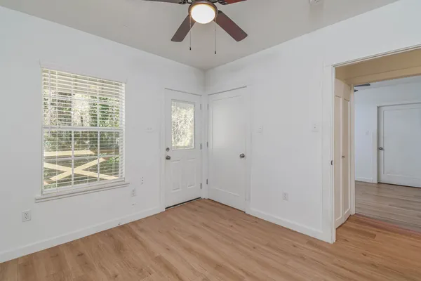 a view of an empty room with wooden floor and a ceiling fan