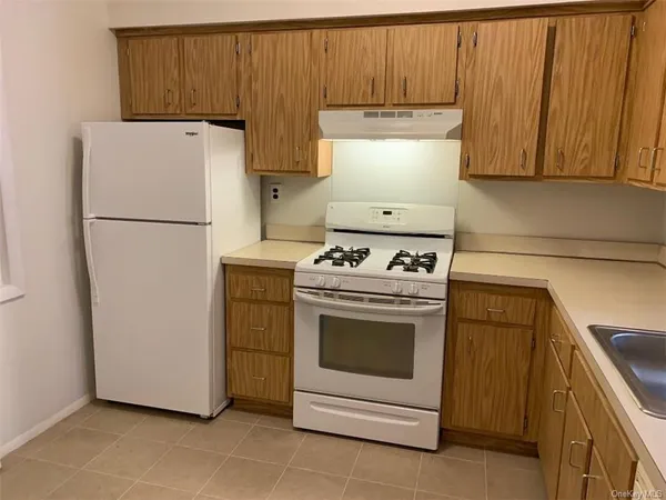 a white refrigerator freezer and a stove sitting inside of a kitchen with granite countertop wooden cabinets