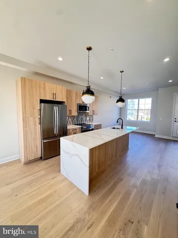 a large kitchen with stainless steel appliances kitchen island granite countertop a refrigerator a sink dishwasher a dining table and chairs with wooden floor