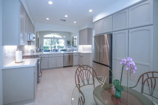 a kitchen with stainless steel appliances granite countertop a refrigerator a sink a stove a dining table and chairs