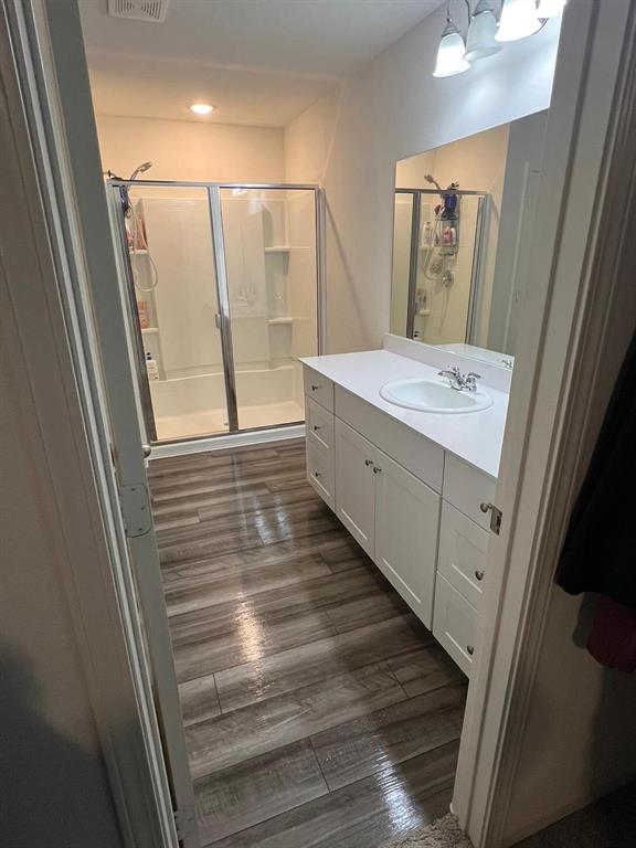 1908 Marquette Road Princeton, TX 75407 - Photo 13 of 14 Bathroom featuring wood-finish flooring, a white vanity with extensive storage, a single basin sink, a large mirror, and a combination tub and shower with sliding glass doors