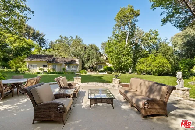 a view of a patio with couches chairs and a fire pit with large trees