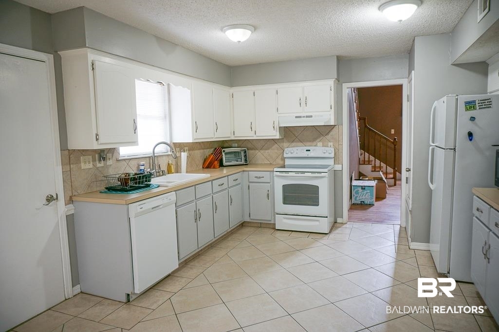254 Thrift Street Mobile, AL 36609 - Photo 9 of 16 Kitchen with a textured ceiling, white appliances, tasteful backsplash, light tile patterned flooring, and light countertops