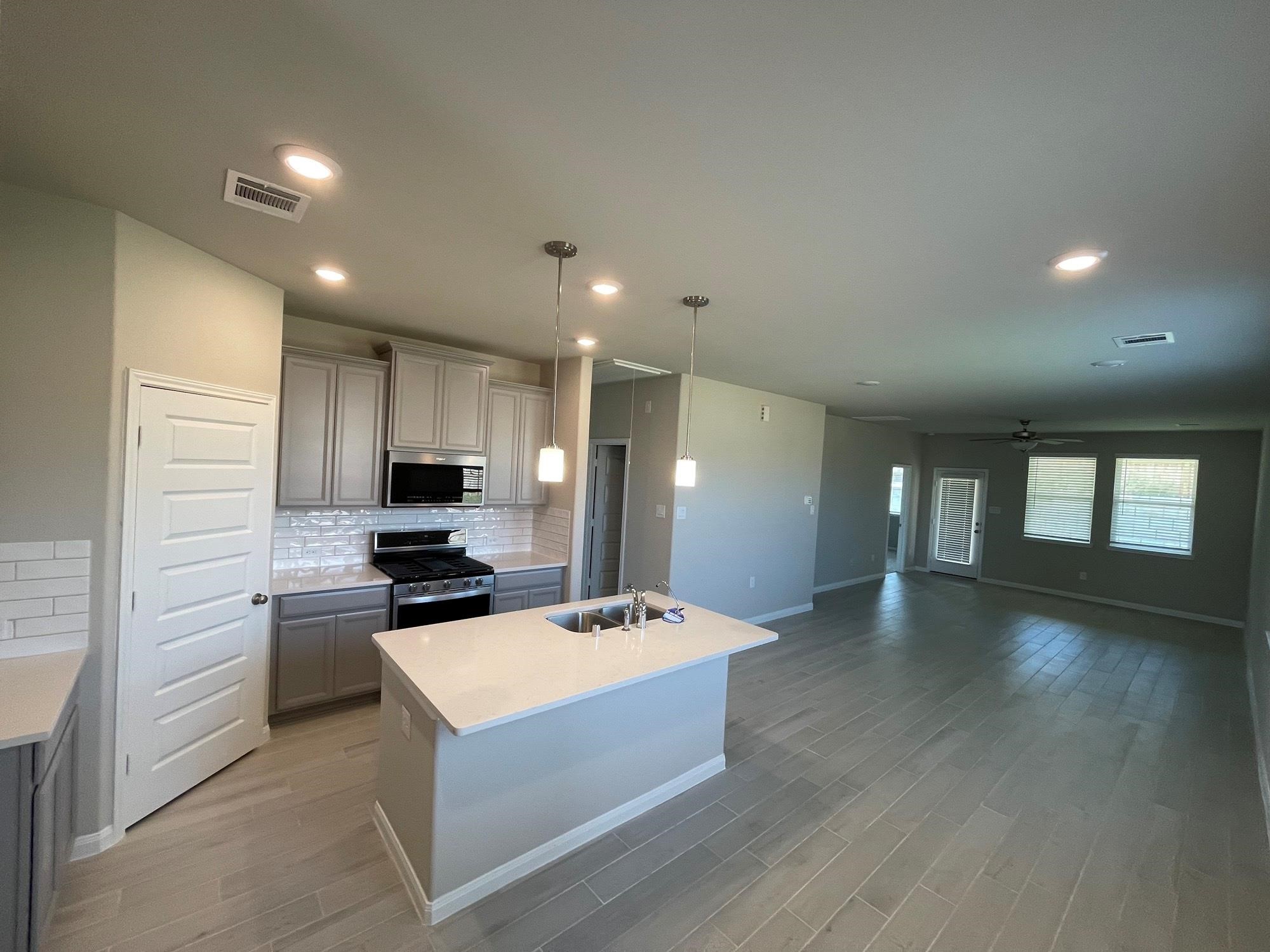 2035 Myrtle Oak Street Conroe, TX 77304 - Photo 6 of 20 a large white kitchen with a refrigerator a stove a sink cabinets and a dining table with wooden floor