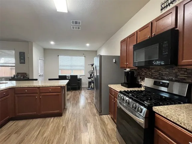 a kitchen with stainless steel appliances granite countertop a stove top oven a sink dishwasher a refrigerator and cabinets with wooden floor