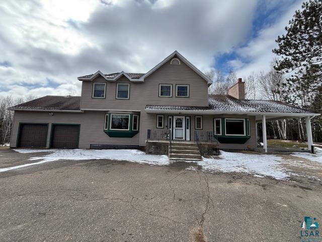 View of front of house featuring a chimney, a garage, driveway, and covered porch