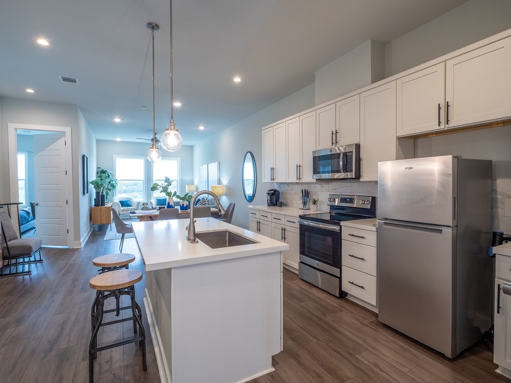 4507 East Martin Luther King Jr Boulevard, Unit 123 Austin, TX 78721 - Photo 25 of 26 Kitchen with open floor plan, appliances with stainless steel finishes, white cabinetry, backsplash, and decorative light fixtures