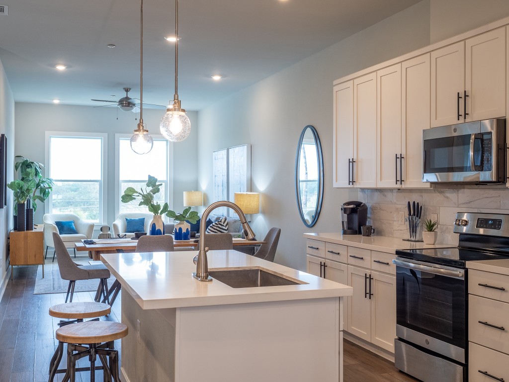 4507 East Martin Luther King Jr Boulevard, Unit 123 Austin, TX 78721 - Photo 26 of 26 Kitchen with appliances with stainless steel finishes, dark wood finished floors, white cabinets, open floor plan, and a kitchen island with sink