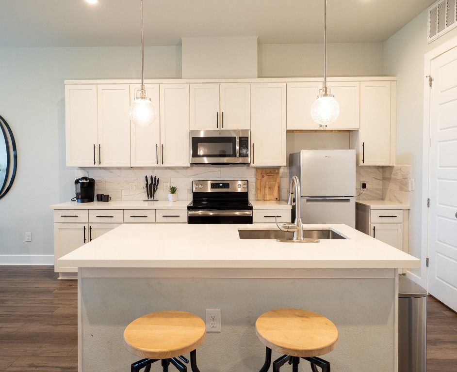 4507 East Martin Luther King Jr Boulevard, Unit 123 Austin, TX 78721 - Photo 4 of 26 Kitchen featuring dark wood-style flooring, appliances with stainless steel finishes, decorative backsplash, a center island with sink, and white cabinets