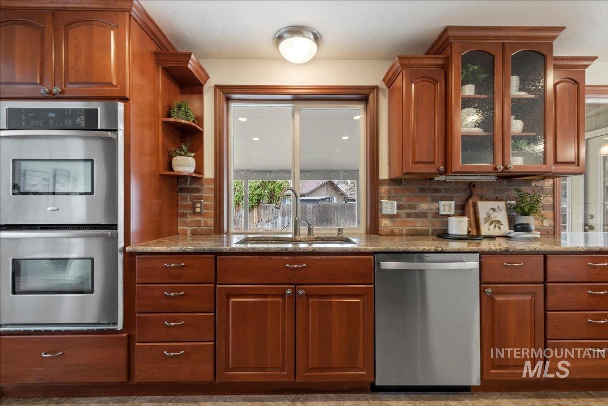 4297 Nystrom Way Boise, ID 83713 - Photo 6 of 50 Kitchen with stainless steel appliances, light stone countertops, wood finish cabinets, brick backsplash, and glass door cabinets