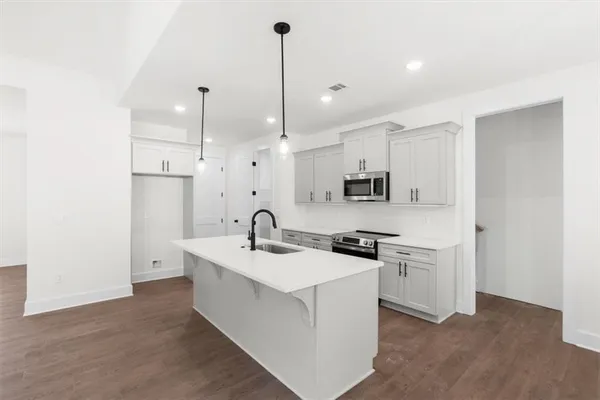 a kitchen with stainless steel appliances granite countertop a sink a stove a refrigerator and white cabinets with wooden floor