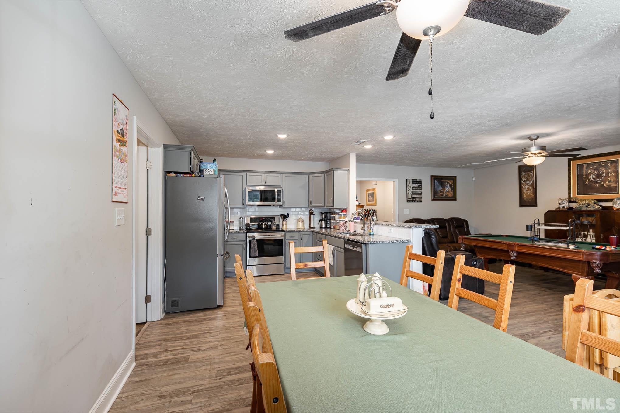 6551 Faircloth Bridge Road Stedman, NC 28391 - Photo 10 of 30 a kitchen with stainless steel appliances kitchen island granite countertop a refrigerator a stove top oven a dining table and chairs with wooden floor