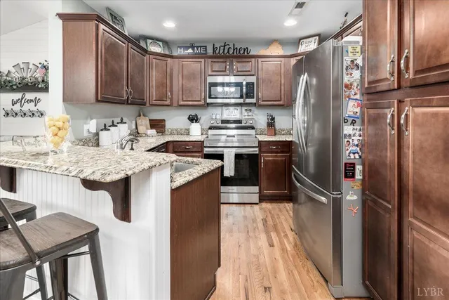 a kitchen with stainless steel appliances granite countertop a refrigerator a stove a sink dishwasher a dining table and chairs with wooden floor
