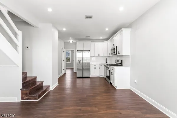 an empty room with wooden floor staircase and windows