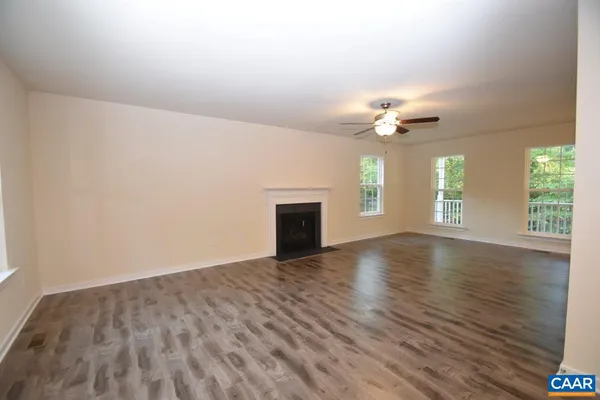 an empty room with wooden floor chandelier fan and windows