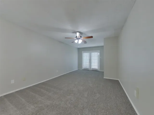 an empty room with chandelier fan and windows