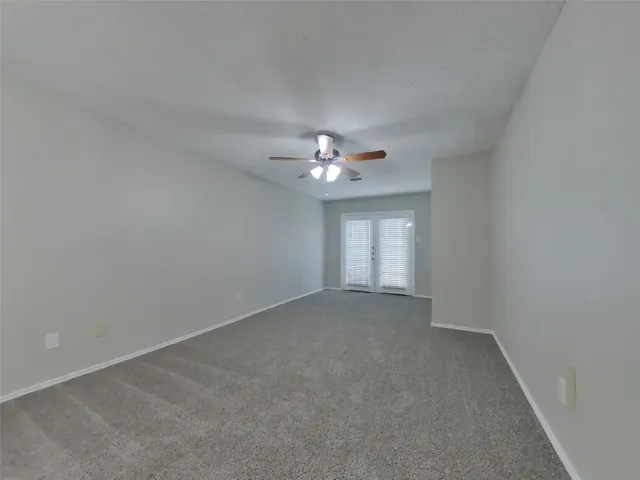 an empty room with chandelier fan and windows