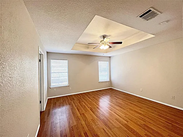 an empty room with wooden floor chandelier fan and windows