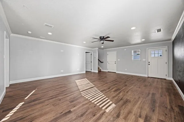 a view of an empty room with wooden floor and a ceiling fan