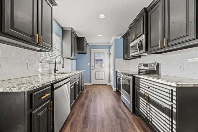 a kitchen with stainless steel appliances granite countertop wooden cabinets a sink and dishwasher a stove top oven with wooden floor