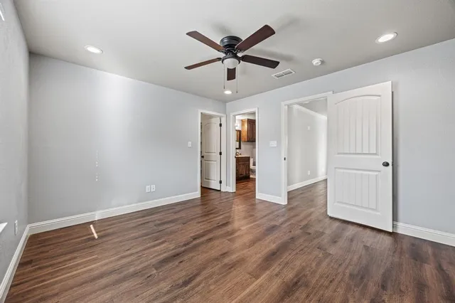 a view of an empty room with wooden floor and a ceiling fan
