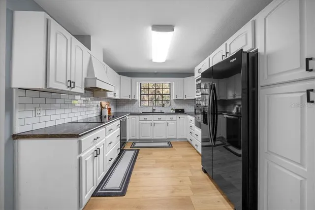 a kitchen with granite countertop a refrigerator a sink dishwasher and white cabinets with wooden floor