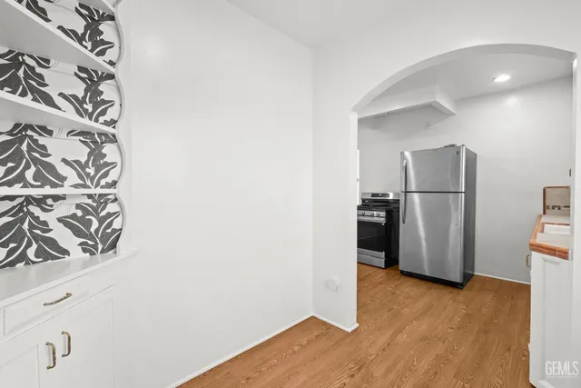 a view of a refrigerator in kitchen and an empty room with wooden floor