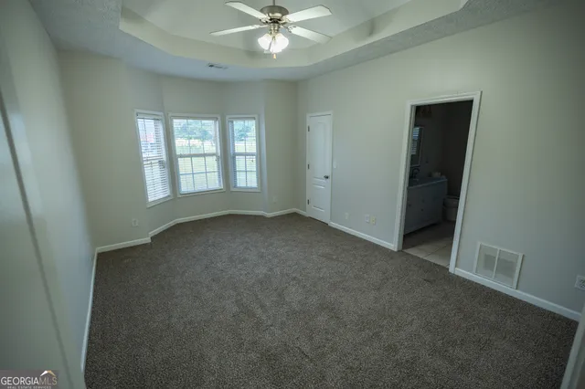 an empty room with chandelier fan and windows