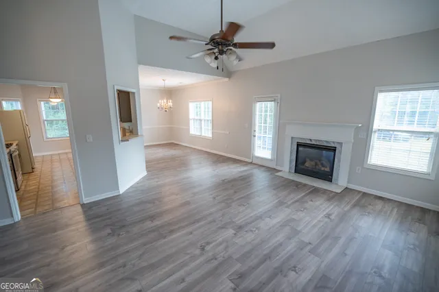 an empty room with wooden floor a chandelier fan and windows