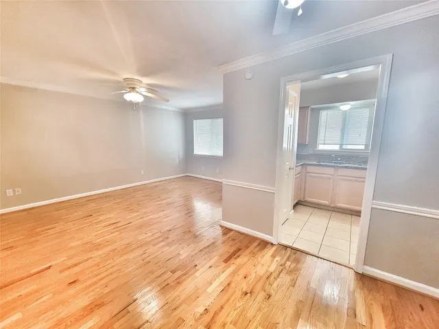 a view of an empty room with wooden floor and a ceiling fan