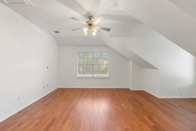 an empty room with wooden floor chandelier fan and windows