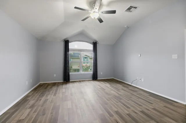 an empty room with wooden floor chandelier fan and windows