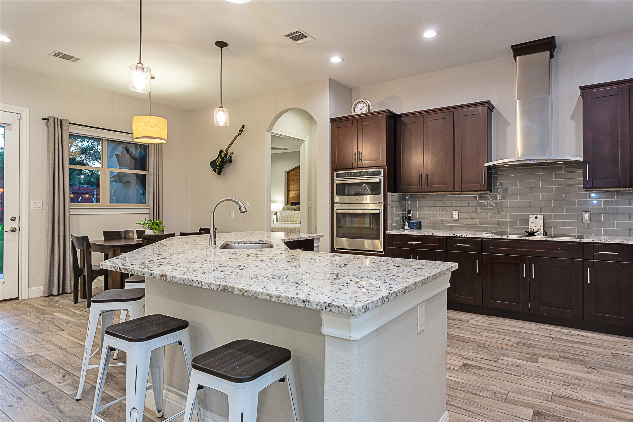 5608 Arroyo Road Austin, TX 78734 - Photo 11 of 39 Kitchen with dark brown cabinetry, wall chimney exhaust hood, decorative light fixtures, light stone counters, and recessed lighting