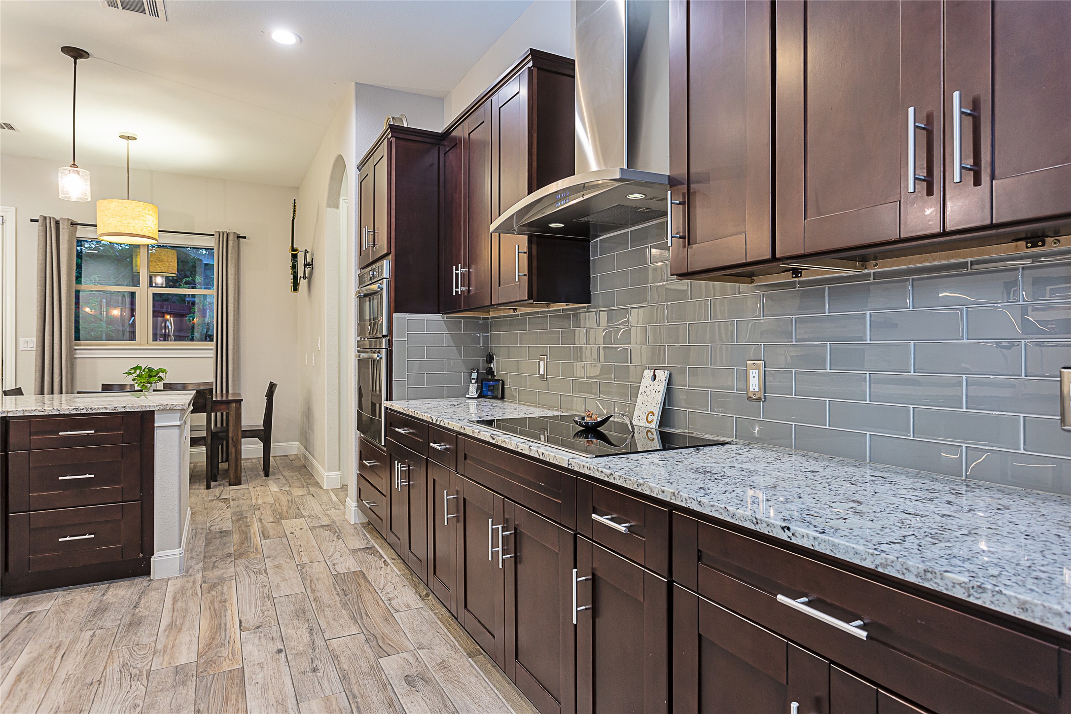 5608 Arroyo Road Austin, TX 78734 - Photo 13 of 39 Kitchen featuring dark brown cabinetry, light stone counters, wall chimney exhaust hood, light wood-style flooring, and decorative light fixtures