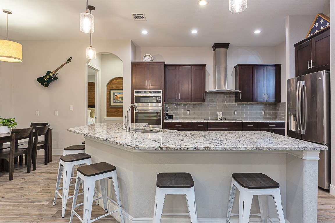 5608 Arroyo Road Austin, TX 78734 - Photo 14 of 39 Kitchen with hanging light fixtures, stainless steel appliances, a breakfast bar, wall chimney exhaust hood, and light wood-style flooring