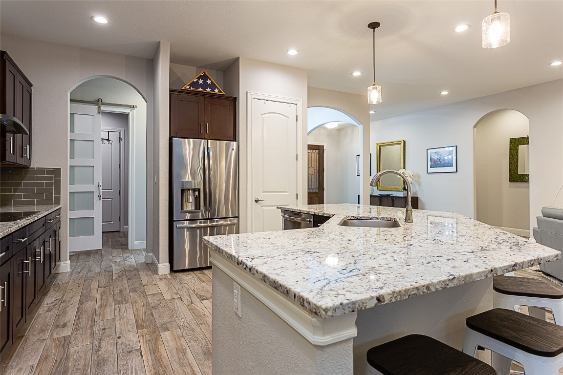 5608 Arroyo Road Austin, TX 78734 - Photo 16 of 39 Kitchen featuring stainless steel appliances, light stone countertops, a barn door, dark brown cabinets, and decorative light fixtures