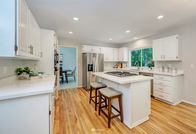 a kitchen with stainless steel appliances kitchen island granite countertop a stove a sink a refrigerator and white cabinets with wooden floor
