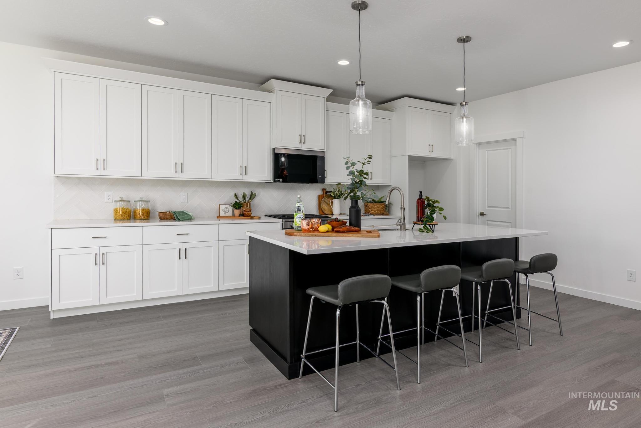 1705 West Paloma Rdg Street Kuna, ID 83634 - Photo 4 of 11 Kitchen featuring dark cabinets, white cabinets, pendant lighting, a kitchen island with sink, and light wood-style floors