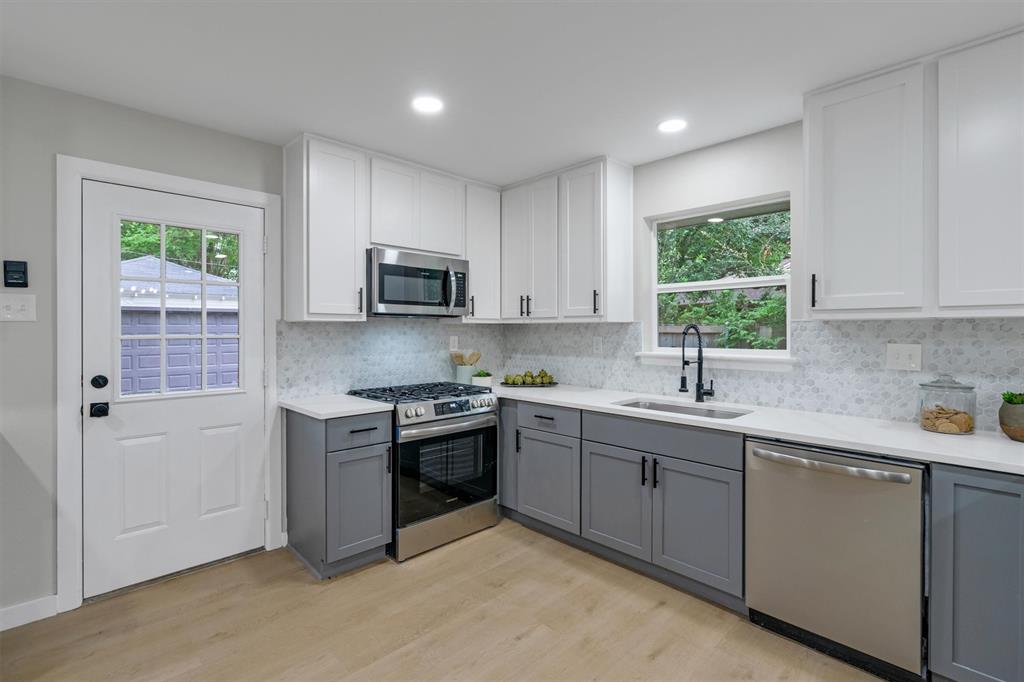 4815 Kelman Street Dallas, TX 75214 - Photo 18 of 37 Modern kitchen featuring two-tone cabinetry, stainless steel appliances, quartz countertops, and a full tile backsplash