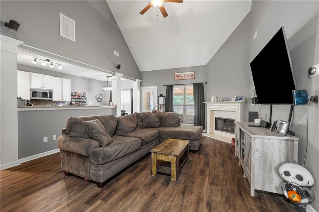 Living room featuring ceiling fan, dark wood-style flooring, a glass covered fireplace, high vaulted ceiling, and ornate columns