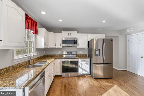 a kitchen with granite countertop a refrigerator a sink dishwasher a stove top oven a refrigerator with wooden floor