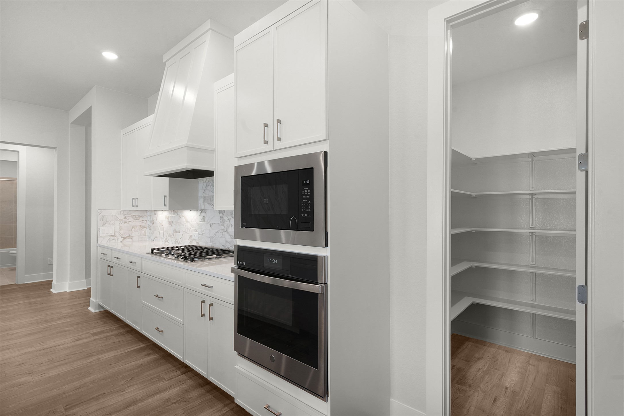 1129 Pansy Trail Georgetown, TX 78628 - Photo 13 of 29 Modern kitchen featuring wood-finish flooring, white cabinetry with silver hardware, and a marble-patterned backsplash