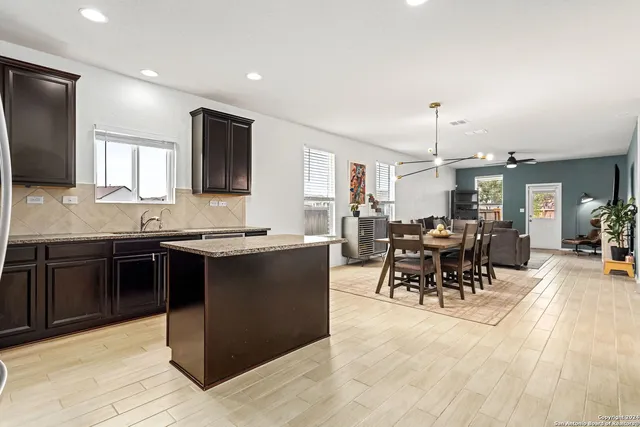 a open kitchen with stainless steel appliances granite countertop a stove top oven a sink a dining table and chairs with wooden floor