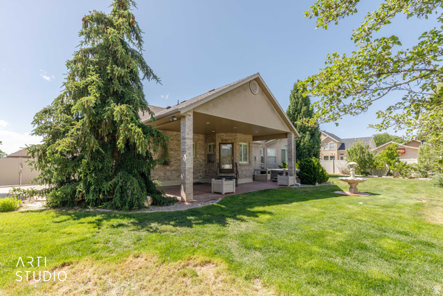 2327 Bluff Ridge Drive Syracuse, UT 84075 - Photo 50 of 66 Expansive backyard featuring a covered patio with brick columns, a decorative fountain, and mature landscaping including a large evergreen tree