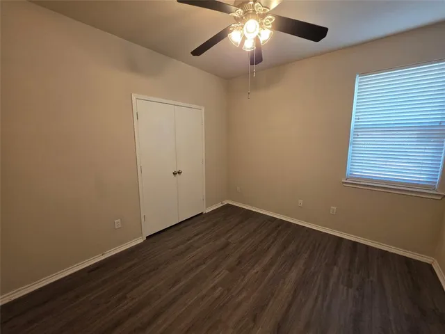 an empty room with wooden floor chandelier fan and windows