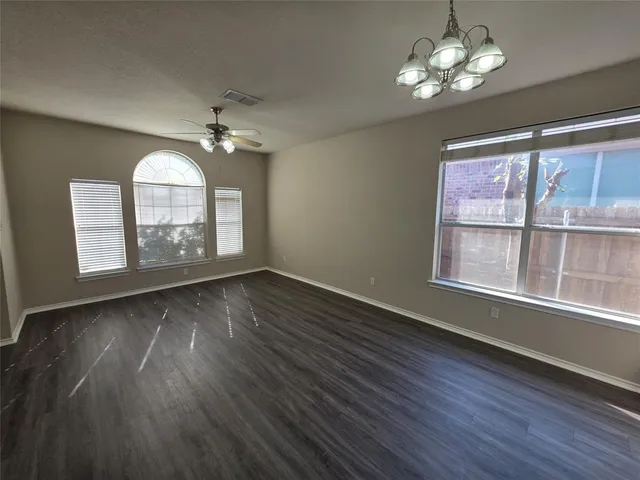 an empty room with wooden floor chandelier fan and windows