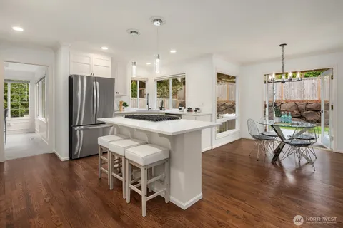 a kitchen with stainless steel appliances granite countertop a stove a refrigerator a kitchen island a dining table and chairs with wooden floor
