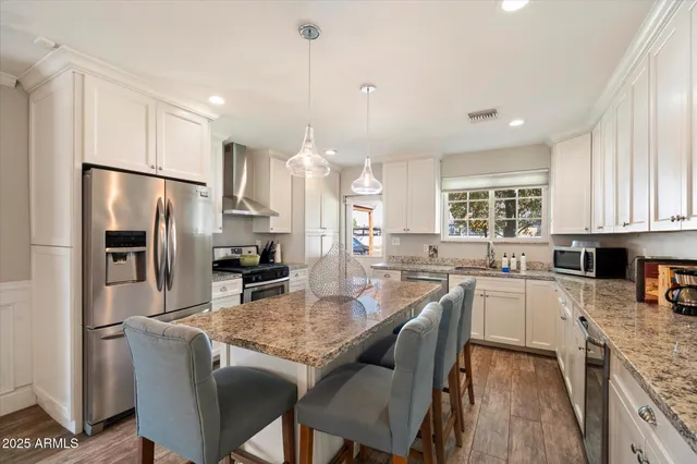 a kitchen with stainless steel appliances granite countertop a refrigerator a stove a sink a dining table and chairs with wooden floor